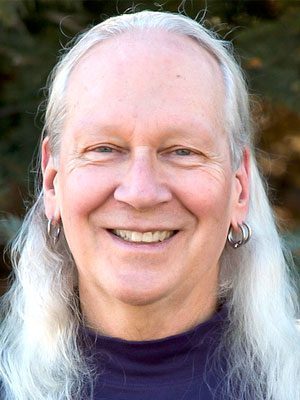 Jim Struve, Light-skinned man with long, silver hair and multiple earrings smiling at the camera.