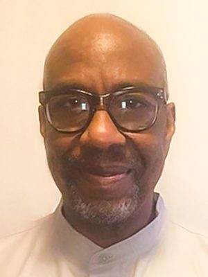 Yao Obiora Dibia, a Bald African American man with glasses in a short-collared beige shit.
